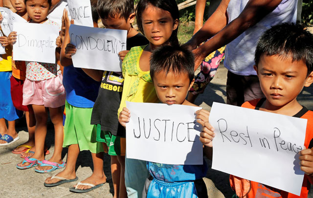 Children display placards as they wait for the convoy transporting the body of Joanna Demafelis, a Filipina domestic helper who was killed and found inside a freezer in Kuwait, to pass by, in her hometown in Iloilo province in the Philippines, on Saturday (Reuters photo)