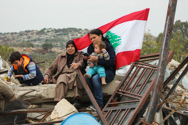 Displaced residents lift a Lebanese flag as they sit on the rubble of their home in their southern Lebanese village of Yarin on January 26, 2025 (AFP photo)