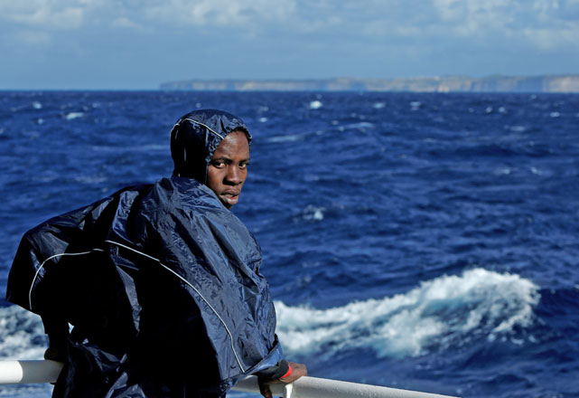 A migrant stands on the deck of the MV Aquarius, a search and rescue ship run in partnership between SOS Mediterranee and Medecins Sans Frontieres, as it passes the Maltese Island of Gozo while making its way to the Italian Island of Sicily after rescue operations in the central Mediterranean off the coast of Libya, on Sunday (Reuters photo)