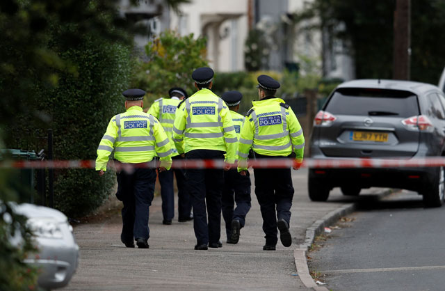 Police officers walk behind cordon tape set up around a property being searched after a man was arrested in connection with an explosion on a London Underground train, in Sunbury-on-Thames, Britain, on Sunday (Reuters photo)