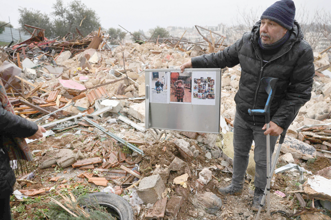 A man on crutches, supporter of the Palestinian Salhiya family, holds pictures by the ruins of the house demolished by Israeli occupation forces in the Sheikh Jarrah neighbourhood on Wednesday (AFP photo)