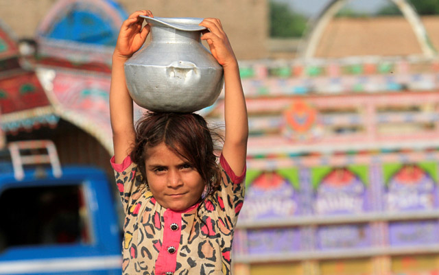 A girl stops to pose for a picture as she carries water home in Peshawar, Pakistan, on Saturday (Reuters photo)