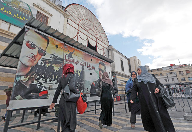 People walk next to a poster depicting Syria's President Bashar Assad in Damascus, Syria, on Tuesday (Reuters photo)