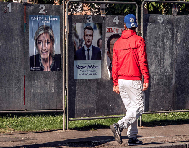 A man walks past a poster showing French presidential election candidate for the far-right Front National Party Marine Le Pen (left) and French presidential election candidate for the En Marche ! movement Emmanuel Macron are plastered along a wall in Henin-Beaumont, north western France, on Wednesday (AFP photo)