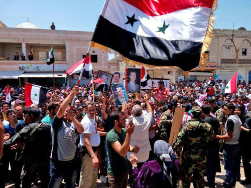 This handout photo released by the official Syrian Arab News Agency on Tuesday shows residents of the town of Harak, east of the Daraa province, carrying national flags and portraits of Syrian President Bashar Assad (AFP photo)