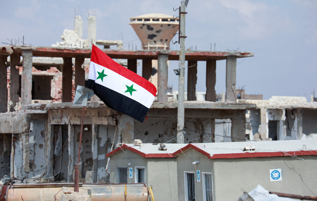 A photo taken during a tour organised by the Syrian ministry of information shows a Syrian flag atop damaged buildings in the district of Daraa Al Balad of Syria's southern city of Daraa, on Sunday (AFP photo)