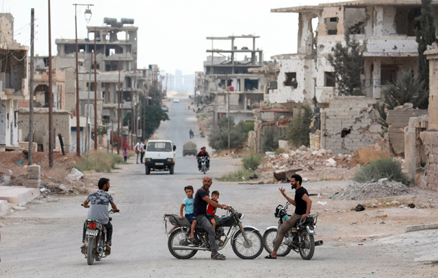 This photo taken during a tour organised by the Syrian Ministry of Information shows locals on motorbikes chatting on a roadside by damaged buildings in the district of Daraa Al  Balad of Syria's southern city of Daraa, on Sunday (AFP photo)