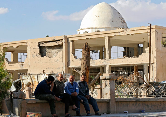 Syrian men sit outside a damaged mosque in the desert town of Al Qaryatain on Sunday after regime forces retook it from the Daesh terror group (AFP photo)