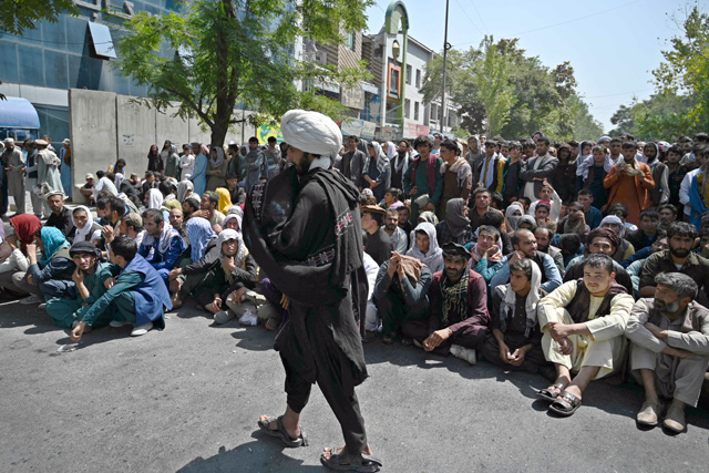A Taliban fighter walks in front of people sitting along a road outside a bank waiting to withdraw money at Shar-e-Naw neighbourhood in Kabul on Saturday (AFP photo)
