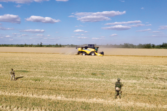 In this aerial photo taken on Thursday, Russian servicemen stand guard in a field as farmers harvest wheat near Melitopol, Zaporizhzhia region, amid the ongoing Russian military action in Ukraine (AFP photo)