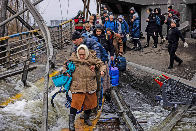 A man helps a woman evacuee cross a destroyed bridge as she and others flee the city of Irpin, northwest of Kyiv, on Monday (AFP photo)