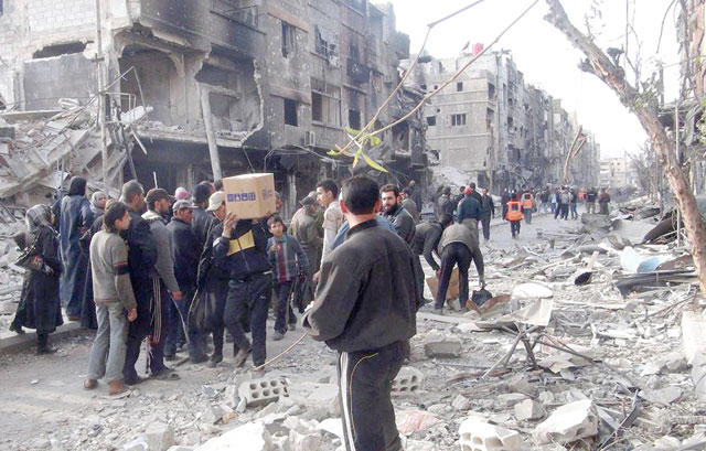 Residents of Syria's besieged Yarmouk Palestinian refugee camp, south of Damascus, stand amidst debris as they wait to receive food parcels on March 24, 2014 (AFP photo)
