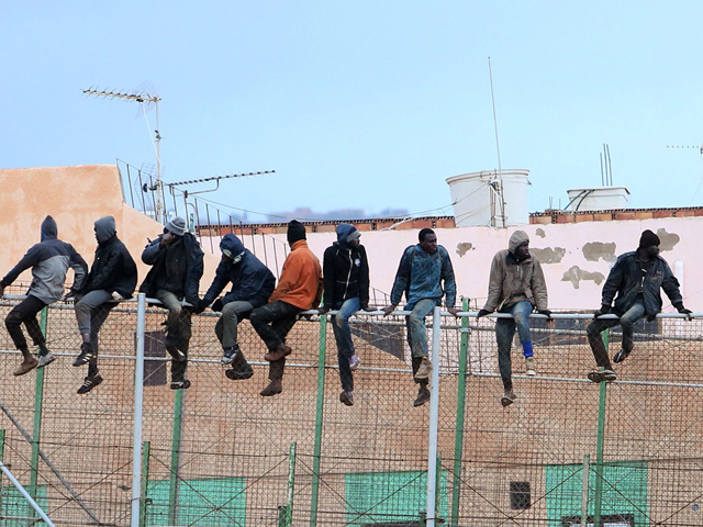 Migrants sit atop a border fence separating Morocco from the north African Spanish enclave of Melilla in the first attempt to jump since the camp on Mount Gurugu burned down on February 19, 2015 (AFP photo)