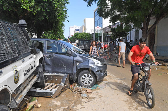 People pass by damaged vehicles near a police station in the Tunisian coastal governorate of Nabeul on Sunday following deadly flash flooding in the town of Bir Challouf (AFP photo)