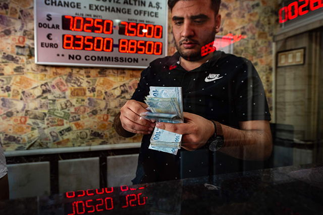 A currency exchange office worker counts Turkish Lira banknotes in front of the electronic panel displaying currency exchange rates at an exchange office in Istanbul, on Thursday as Turkey's lira set a new record low against the US dollar (AFP photo)