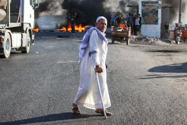 An elderly Iraqi man walks with a cane past protesters burning tyres as they block the main road between the centre of the southern city of Basra leading towards Karmat Ali on its northern outskirts on Monday (AFP photo)
