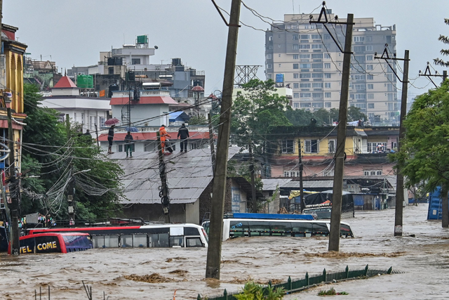 Residents climb over a rooftop as their neighbourhood submerged in flood waters after the Bagmati River overflowed following heavy monsoon rains in Kathmandu on September 28 (AFP photo)