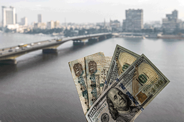 Two pairs of US hundred dollar and Egyptian hundred pound notes are held before a window showing the skyline of Egypt's capital Cairo and the Nile River on Monday (AFP photo)