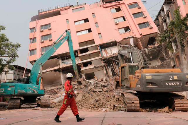 A rescue worker walks past heavy construction equipment being used to clear rubble at the site of a collapsed building in Mandalay today following the March 28 earthquake (AFP photo)