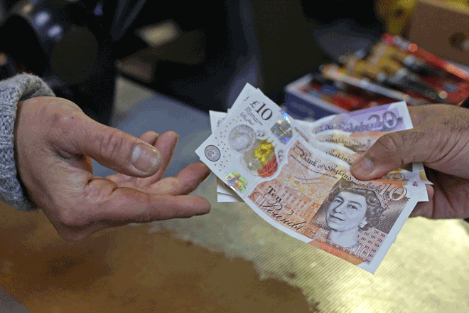 A shopkeeper passes a customer their change in GBP pound sterling ten and twenty pound notes, at a shop in east London on Friday  (AFP photo)