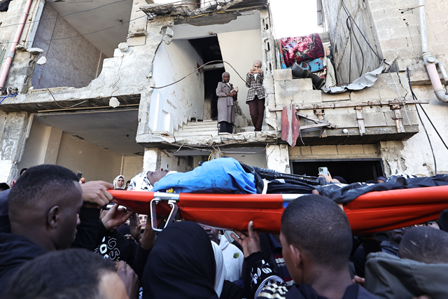 Women take pictures from a damaged building as mourners carry the body of one of the Palestinians, who were killed during a days-long Israeli raid, during their funeral in a refugee camp in Tulkarm in the occupied West Bank on Friday (AFP photo)
