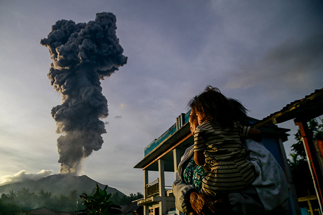 A woman and child look on at volcanic ash rising into the air during the eruption of Mount Ibu, as seen from Duono Village in West Halmahera, North Maluku province, on January 15, 2025 (AFP photo)
