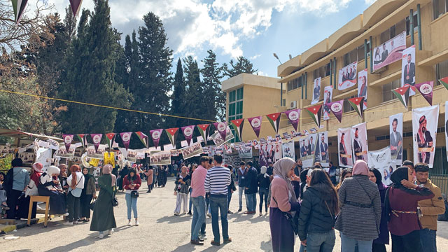 University of Jordan students line up at the polls to vote for their student council representatives, on Thursday. The many banners and posters seen in the background caused some students to allege outside funding (Photo by Maram Kayed)