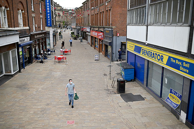 In this file photo taken on June 16, 2021 a pedestrian wearing a face covering due to Covid-19 walks past closed-down shops in Blackburn, north west England on June 16, 2021 (AFP photo)