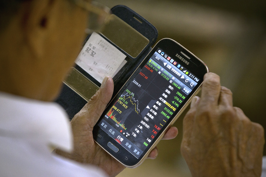 A Chinese investor uses his smartphone to monitor stock prices at a brokerage house in Beijing, on Tuesday (AP photo)