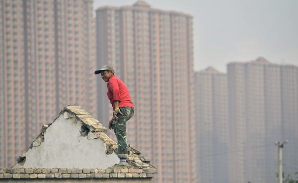 A man stands on the top of a building as farmers’ houses are demolished to make space for new property to be built, in front of a residential compound in Hefei, Anhui province, in this October 19, 2013 file photo (Reuters photo)