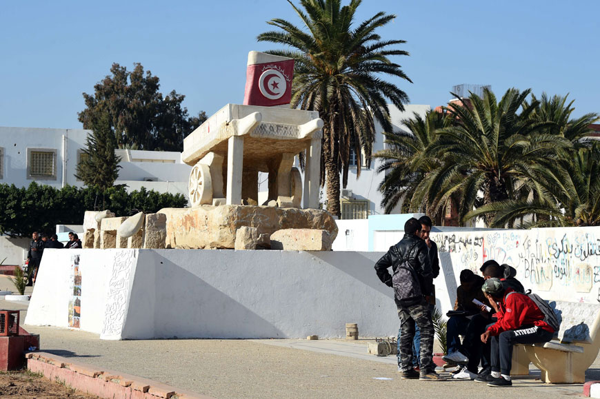Tunisian youths sit next to a sculpture featuring a cart and symbolising poverty on Mohamed Bouazizi Square on Monday, in the central town of Sidi Bouzid, three days ahead of the fifth anniversary of the self-immolation of Mohamed Bouazizi, a young street vendor, which sparked the revolution that ousted a dictator and ignited the Arab Spring (AFP photo)