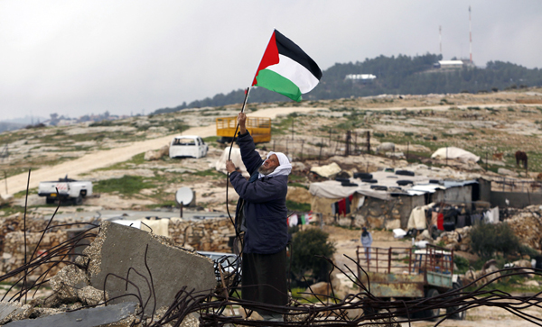 A Palestinian man hangs a Palestinian flag atop the ruins of a mosque, during a snow storm in West Bank village of Mufagara, south of Hebr, onWednesday (Reuters photo)