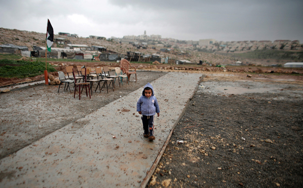 A Palestinian bedouin child from the Abu Anwar community runs to take cover during a rainfall as he attends a class in the West Bank city of Al Azariya near the Jewish settlement of Maale Adumim (background), East of Jerusalem, on Tuesday (AFP photo)
