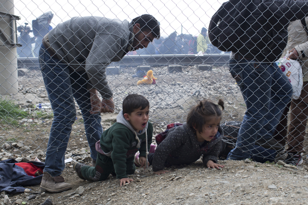 A man helps children to run away after police in the Former Yugoslav Republic of Macedonia (FYRM) fired tear gas at a group of the refugees and migrants who tried to push their way into the FYRM, breaking down a border gate near the northern Greek village of Idomeni on Monday (AP photo)