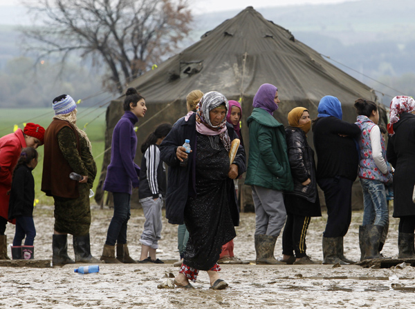 A refugee woman walks through the mud, carrying tea and bread as others are waiting in line, in a makeshift camp at the northern Greek border post of Idomeni, on Wednesday (AP photo)