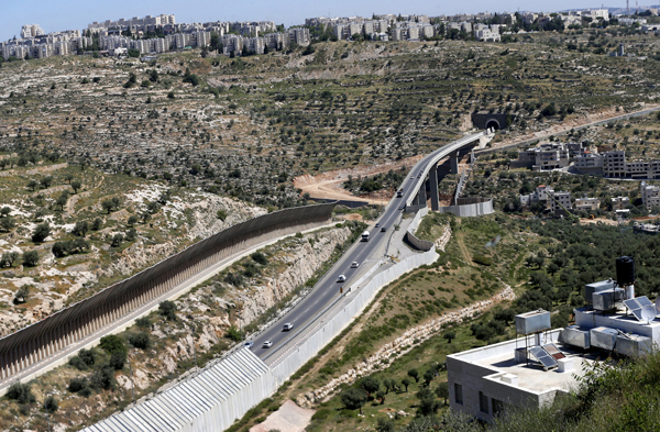 Cars drive on a road where workers construct a section of the Israel’s separation barrier in the West Bank city of Beit Jala, near Bethlehem, on Monday (Reuters photo)