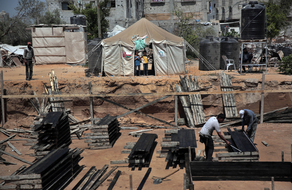 In this July 23, 2015, photo, two Palestinian boys stand outside a tent (background) watching workers rebuild a house which was destroyed during the 2014 summer war between Israel and Hamas, as the long-awaited reconstruction began in Shijaiyah neighbourhood, eastern Gaza City (AP photo)