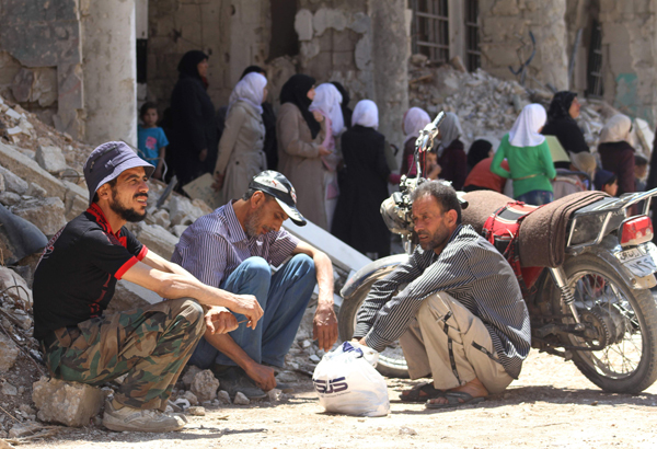Syrian men sit next to a damaged building in the town of Daraya, southwest of central Damascus, on Sunday (AFP photo)