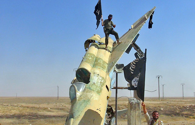 In this undated file image posted by the Raqqa Media Centre, militants wave the Daesh’s flag from a damaged display of a government fighter jet following the battle for the Tabaqa air base (AP photo)