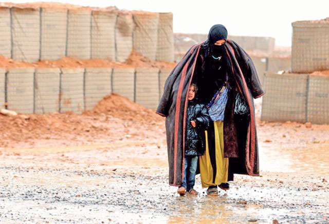 In this file photo taken on March 1, 2017, a Syrian refugee from the informal Rukban camp, which lies in no-man's-land off the border between Syria and Jordan in the remote northeast, walks in the rain as she shelters a young child outside a UN-operated medical clinic immediately on the Jordanian side  (AFP file photo)