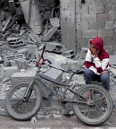 A young Palestinian boy sits next to his bicycle in front of a building hit by overnight Israeli bombardment in Rafah in the southern Gaza Strip on Sunday (AFP photo)