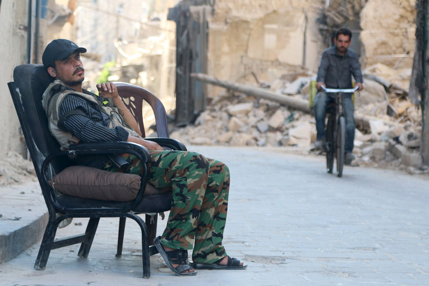 A Free Syrian Army fighter sits at a checkpoint as a man rides a bicycle past the rubble of a damaged building in the old city of Aleppo, on Monday (Reuters photo)
