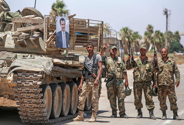Syrian soldiers stand flashing the victory gesture next to a photo of Syrian President Bashar Assad hanging on a tank at the Nassib border crossing with Jordan in the southern province of Daraa on Saturday (AFP photo)