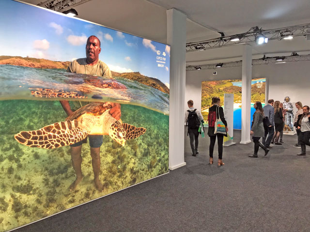 Delegates walk past a poster showing a man holding a turtle and other photos from the Pacific Islands during the COP23 UN Climate Change Conference 2017, hosted by Fiji but held in Bonn, Germany, on Friday (Reuters photo)