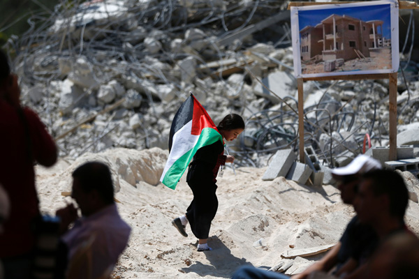 A Palestinian child holds a national flag as she walks past the rubble of the Palestinian homes that were destroyed by Israeli authorities during the Friday prayer in the village of Qalandia (AFP photo)