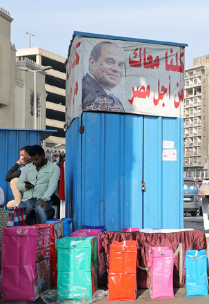 A gift bags vendor waits for customers near a campaign poster of Egypt's President Abdel Fattah Al Sisi that reads: ‘All of us with you’, in Cairo, Egypt, on Tuesday (Reuters photo)