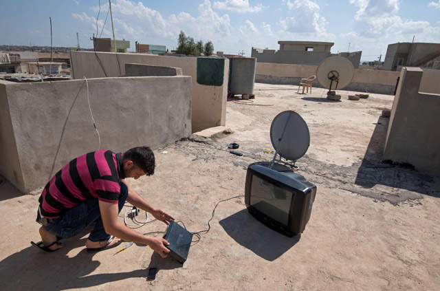 Mohammad Turki installs a satellite dish on the rooftop of a house in eastern Mosul's Al Qahira district on April 15 (AFP photo)