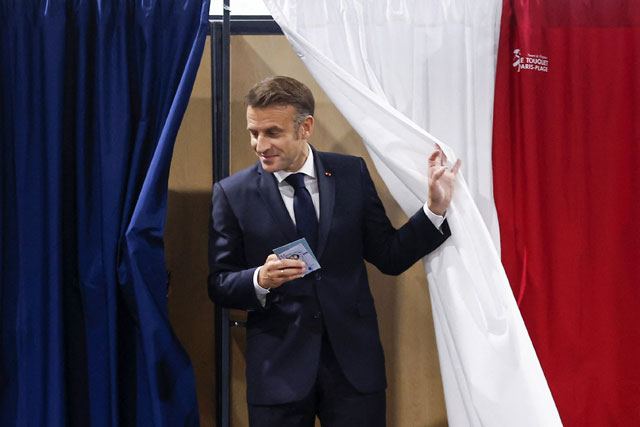 France's President Emmanuel Macron exits a polling booth, adorned with curtains displaying the colors of the flag of France, to vote in the second round of France's legislative election at a polling station in Le Touquet, northern France on Sunday (AFP photo)