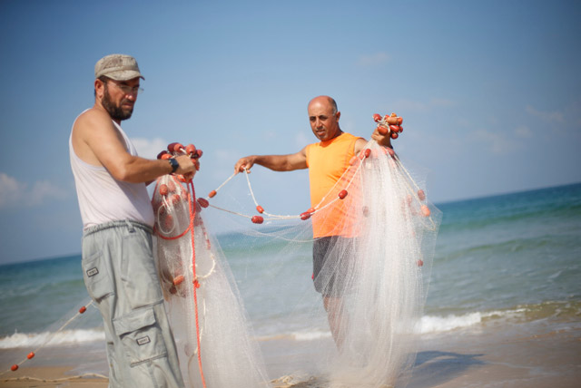 Palestinian fisherman Jihad Al Soltan (right) prepares his fishing net on a beach in the northern Gaza Strip on Monday (Reuters photo)