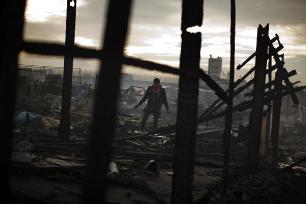 A migrant looks at the remains of a shop burnt in the makeshift migrant camp near Calais, northern France, on October 26 (AP photo)